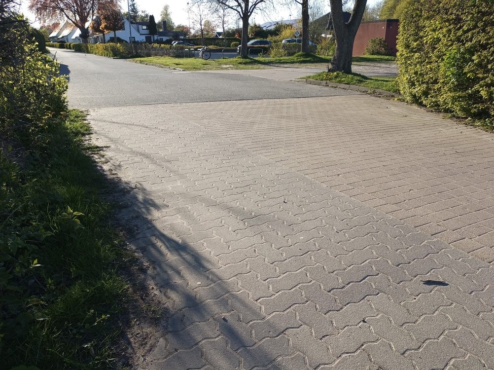 The Ultimate Guide to Interlocking Driveway Designs for Modern Homes. Interlocking paver driveway meeting a residential street with long afternoon shadows.